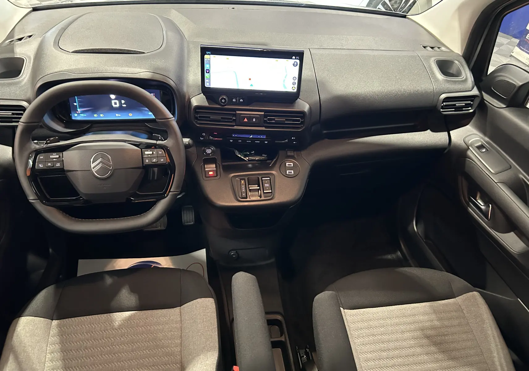 Vue intérieure avant du Citroën Berlingo Multispace 2026, tableau de bord noir avec écran tactile central et sièges bicolores tissu.