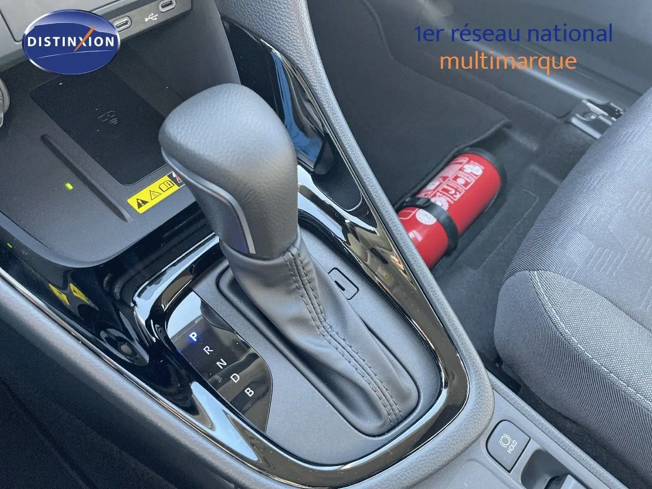 Le levier de vitesses automatique noir de la Toyota Yaris Hybrid 116ch vu en gros plan côté conducteur avec extincteur rouge visible.