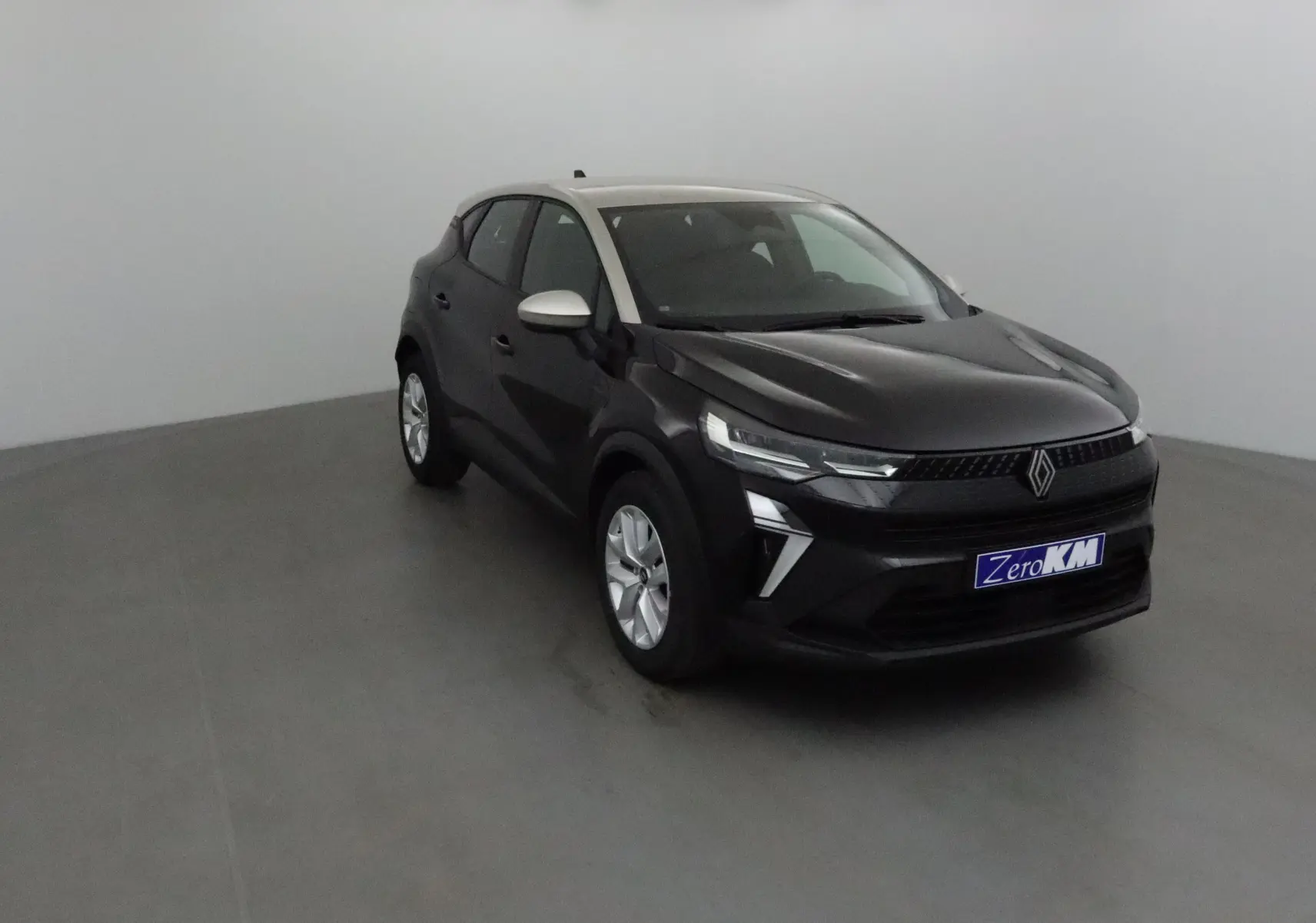 Renault Captur 2025 noir et gris perle en 3/4 avant droit, avec signature lumineuse LED et calandre noire distinctive.