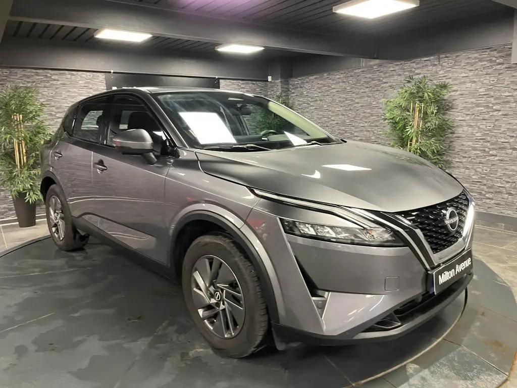 Nissan Qashqai gris 3/4 avant droit en intérieur, avec calandre noire et phares LED étirés.