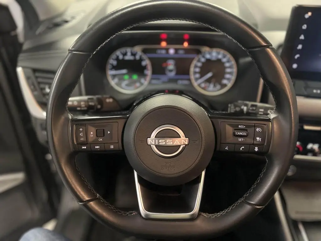 Volant cuir noir du Nissan Qashqai 1.3 Mild Hybrid 2023 avec commandes intégrées et tableau de bord numérique flou.