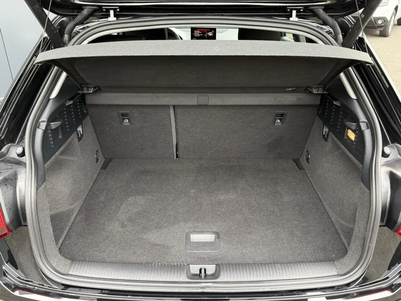Coffre ouvert vu de face d'un Audi Q2 noir métallisé 2023 avec hayon électrique et intérieur de coffre gris.