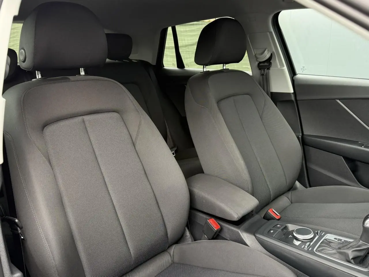 Intérieur de l'Audi Q2 2023 en vue rapprochée des sièges avant en tissu gris avec console centrale et levier de vitesses automatique.