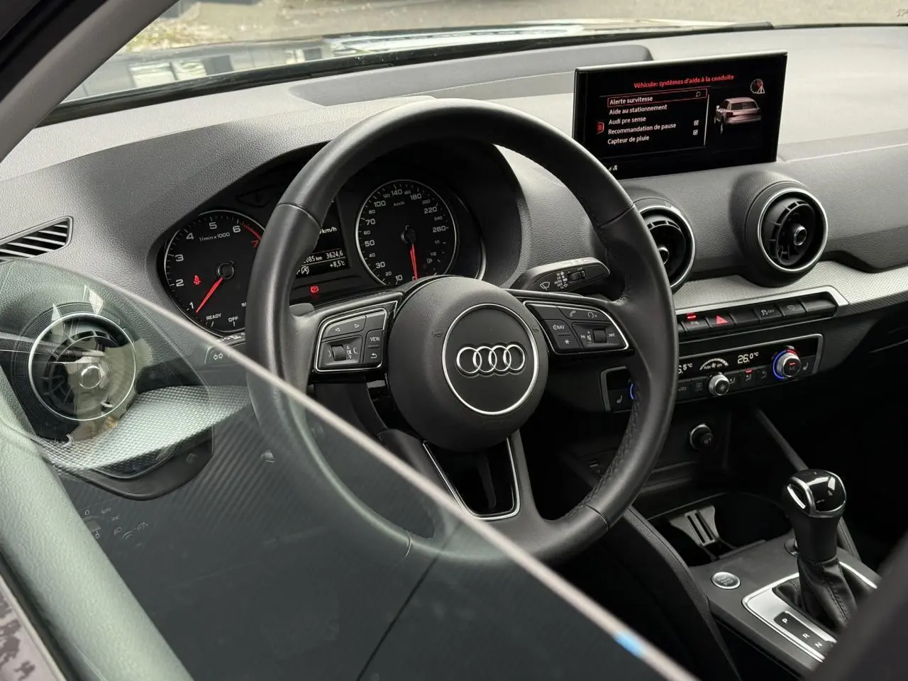 Vue intérieure de l'Audi Q2 2023 S line, tableau de bord noir avec volant multifonction et écran central tactile.