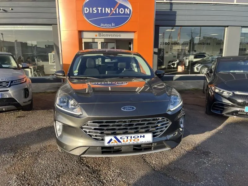 Vue frontale d’un Ford Kuga 2.0 EcoBlue 150ch mHEV Titanium gris Magnetic métallisé, stationné devant un concessionnaire.