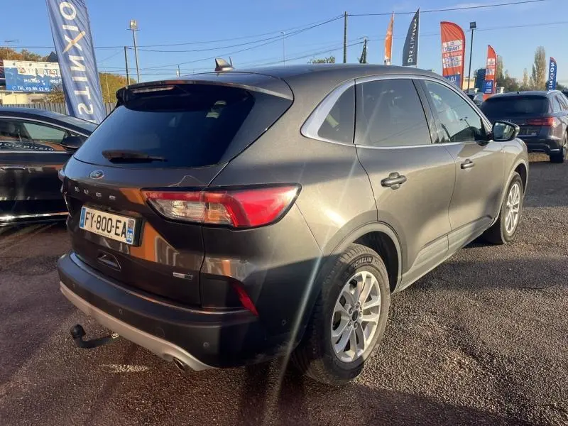 Vue 3/4 arrière droit d'un Ford Kuga 2.0 EcoBlue gris métallisé avec barres de toit et attelage visible.