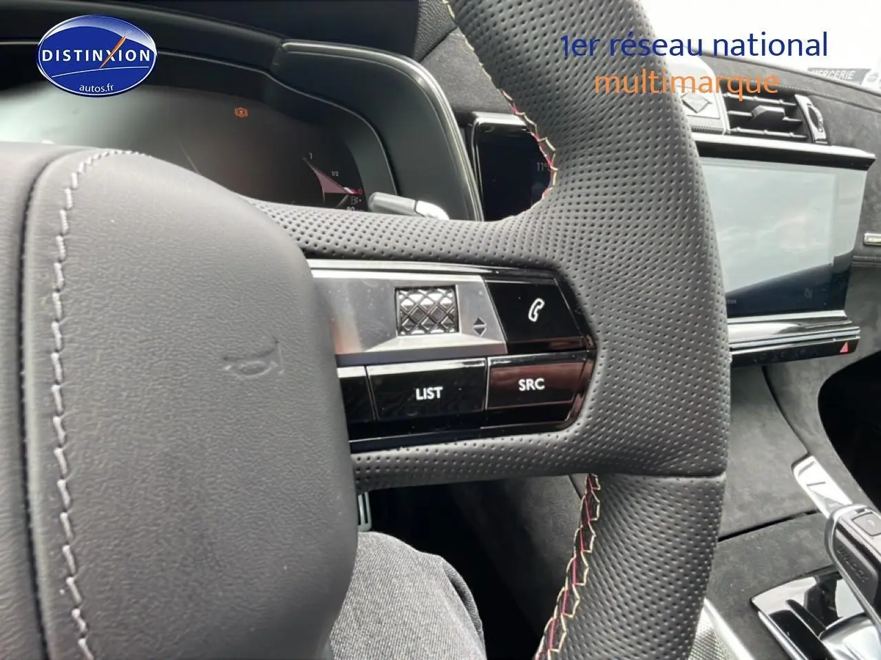 Gros plan sur le volant en cuir perforé avec commandes intégrées du DS7 gris titane, tableau de bord et écran tactile visibles.