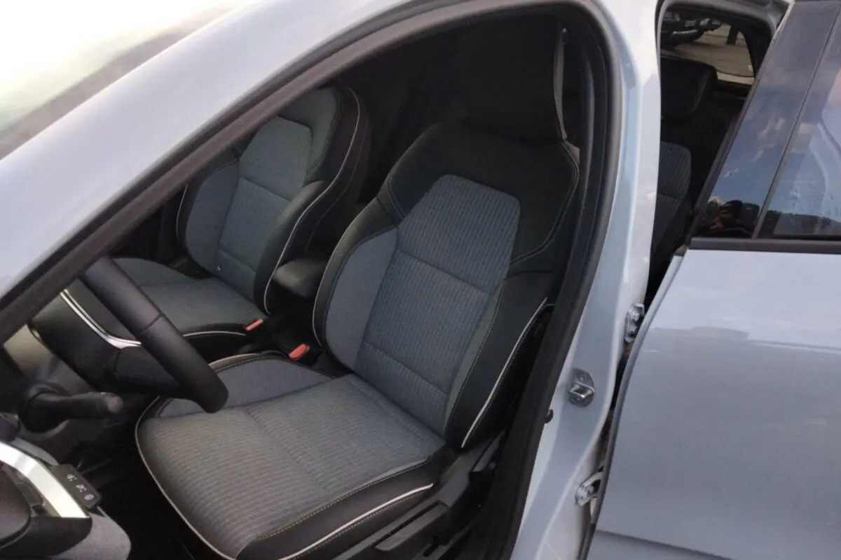 Vue intérieure côté conducteur de la Renault Clio gris rafale 2025, montrant les sièges en tissu et cuir avec surpiqûres blanches.