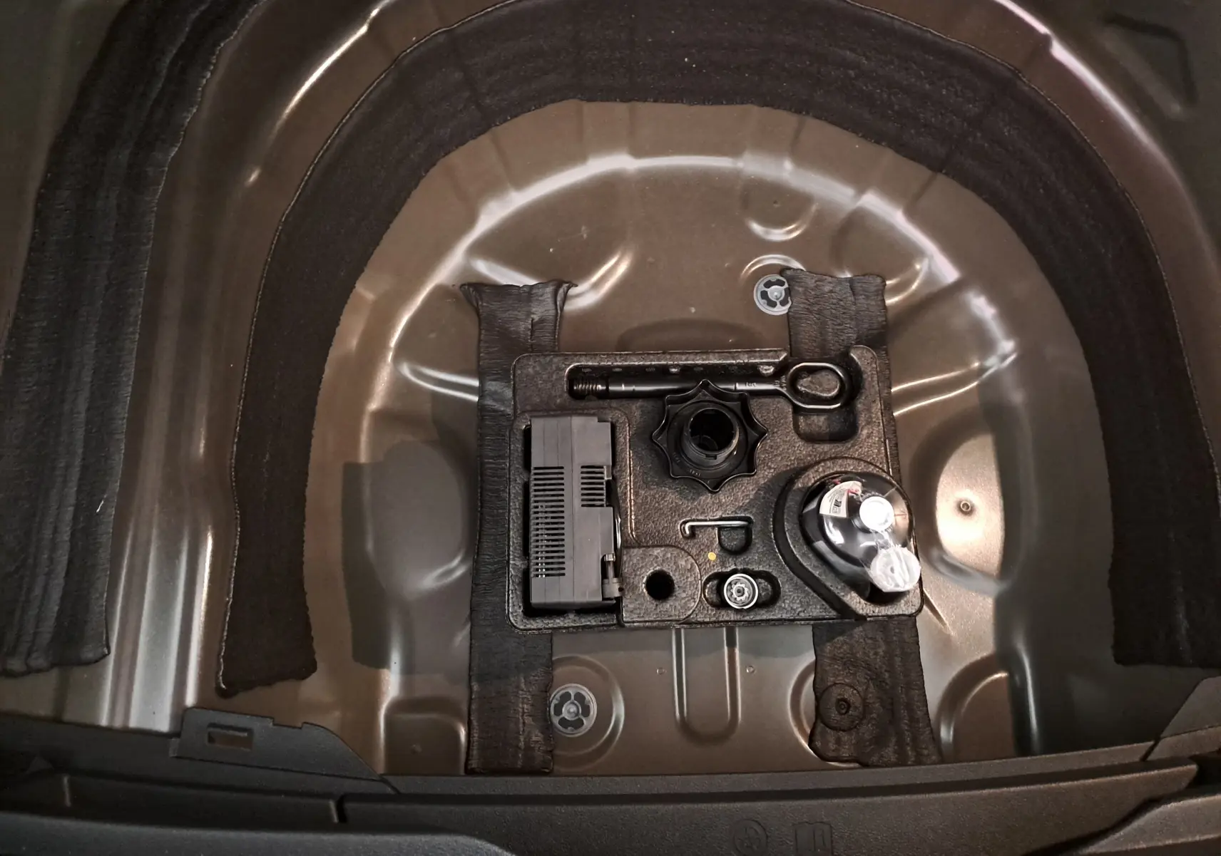 Vue plongeante sur le coffre ouvert d'un Volkswagen Taigo 2025 noir intense nacré, montrant le rangement pour outils et compresseur.