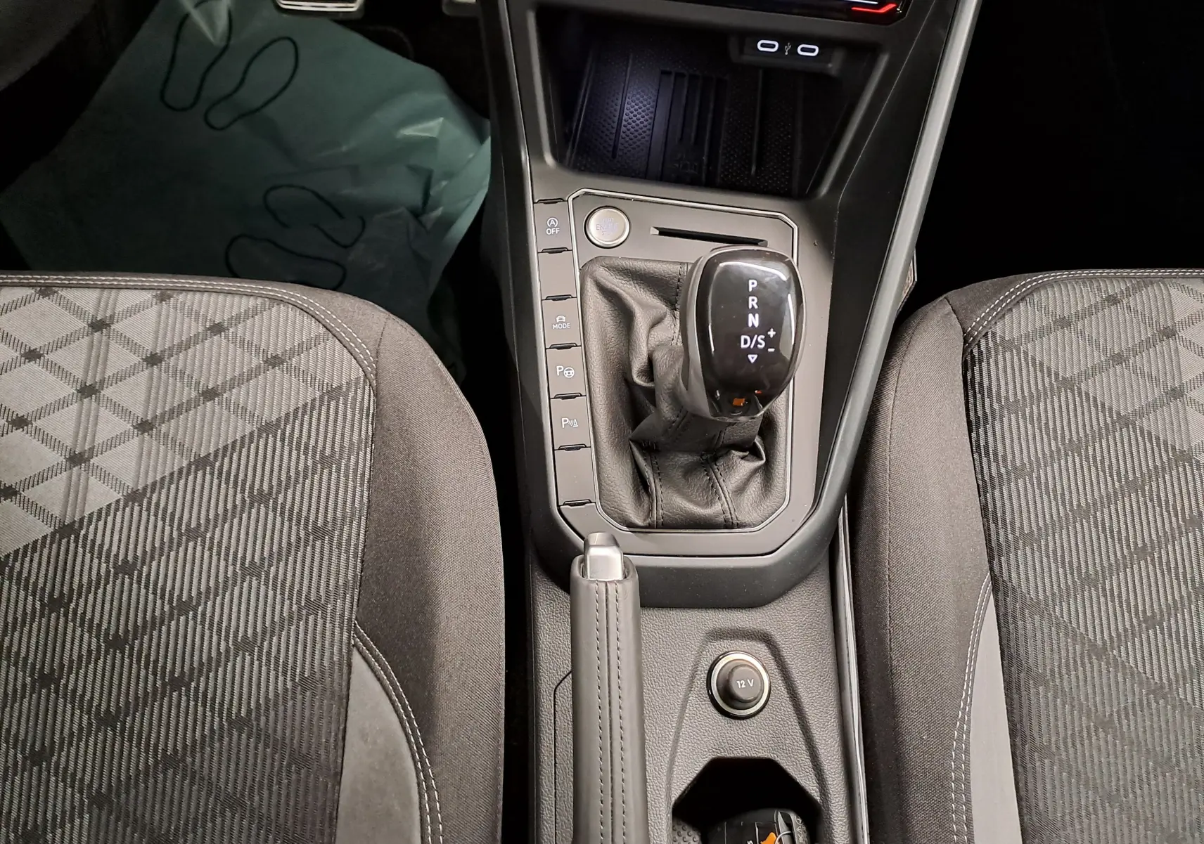 Vue rapprochée du levier de vitesse automatique et frein à main cuir entre les sièges avant gris à motifs du Volkswagen Taigo 2025.