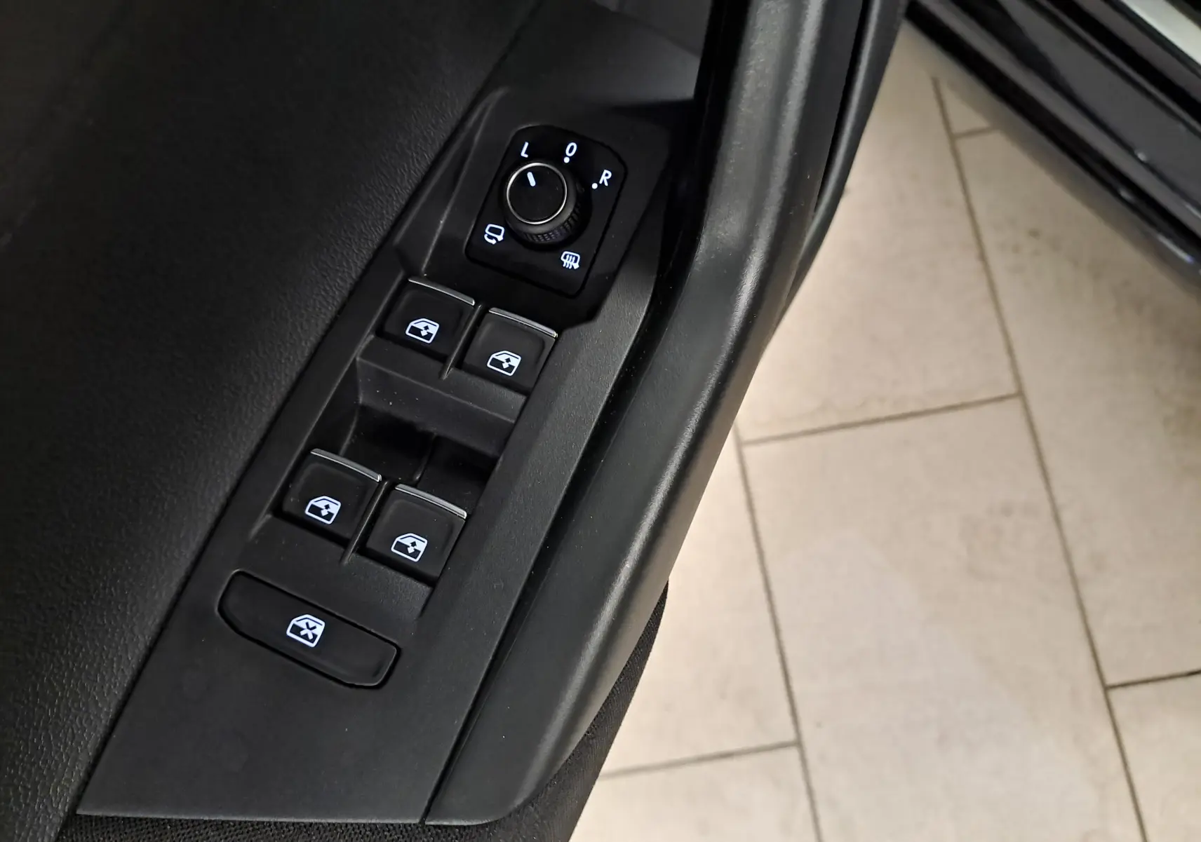 Gros plan sur les commandes de lève-vitres et réglage des rétroviseurs côté conducteur du Volkswagen Taigo noir intense nacré.