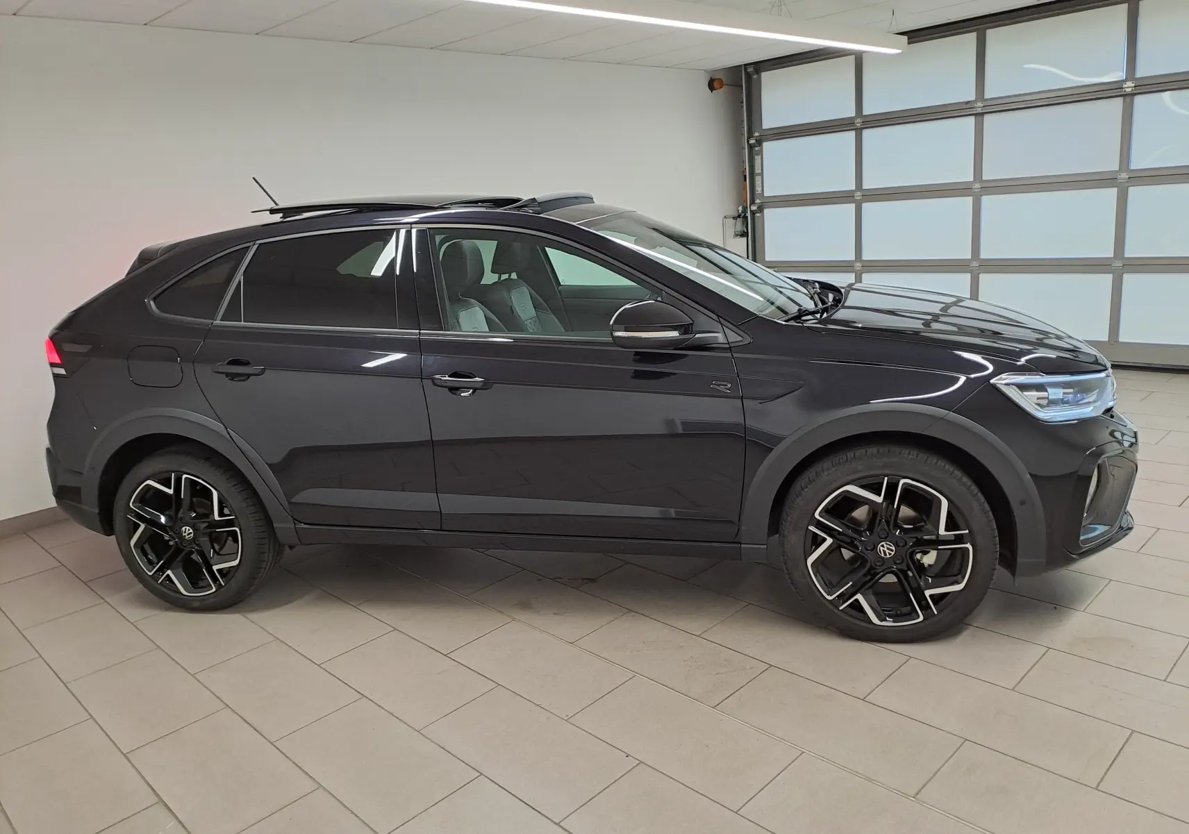 Profil droit d'un Volkswagen Taigo noir intense nacré avec jantes alliage et toit ouvrant en intérieur showroom.