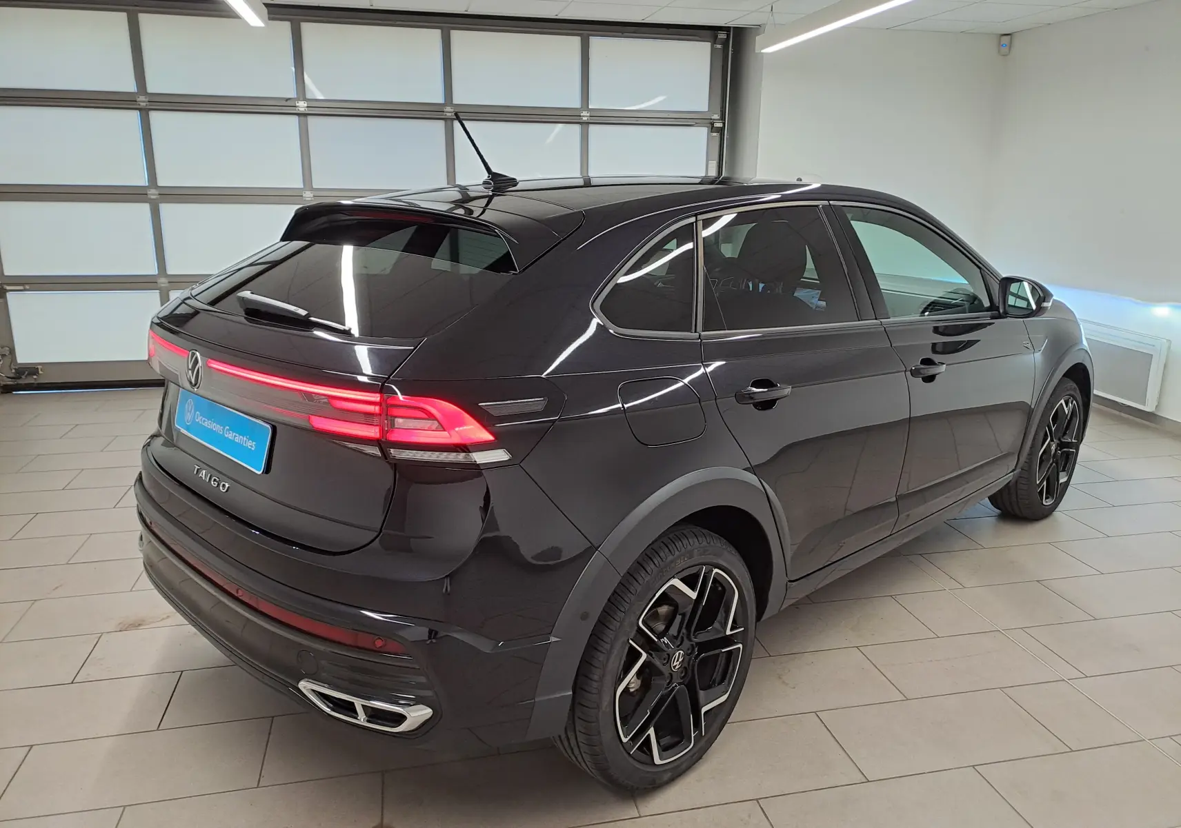 Vue 3/4 arrière droite du Volkswagen Taigo noir intense nacré avec jantes alliage et feux arrière LED allumés.