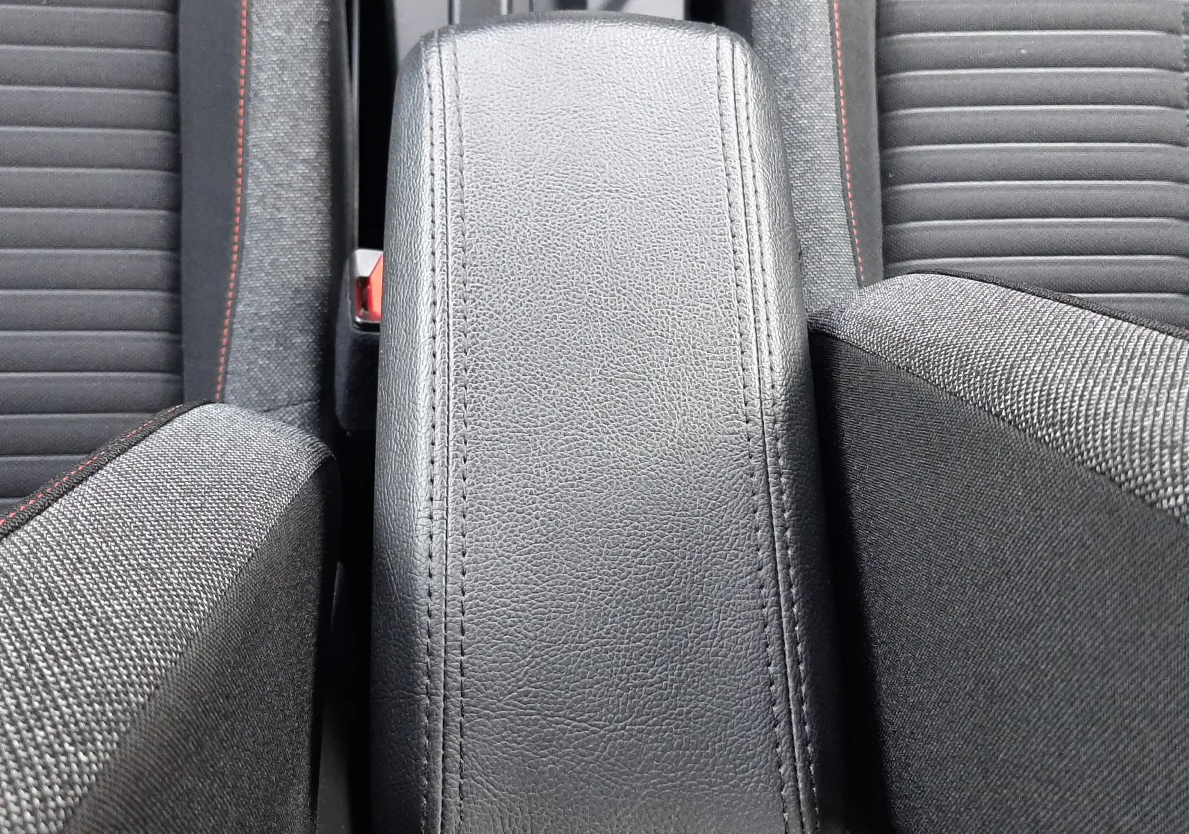 Vue plongeante sur l'accoudoir central en cuir noir et les sièges tissu noir avec surpiqûres rouges d'un Peugeot 2008 blanc.