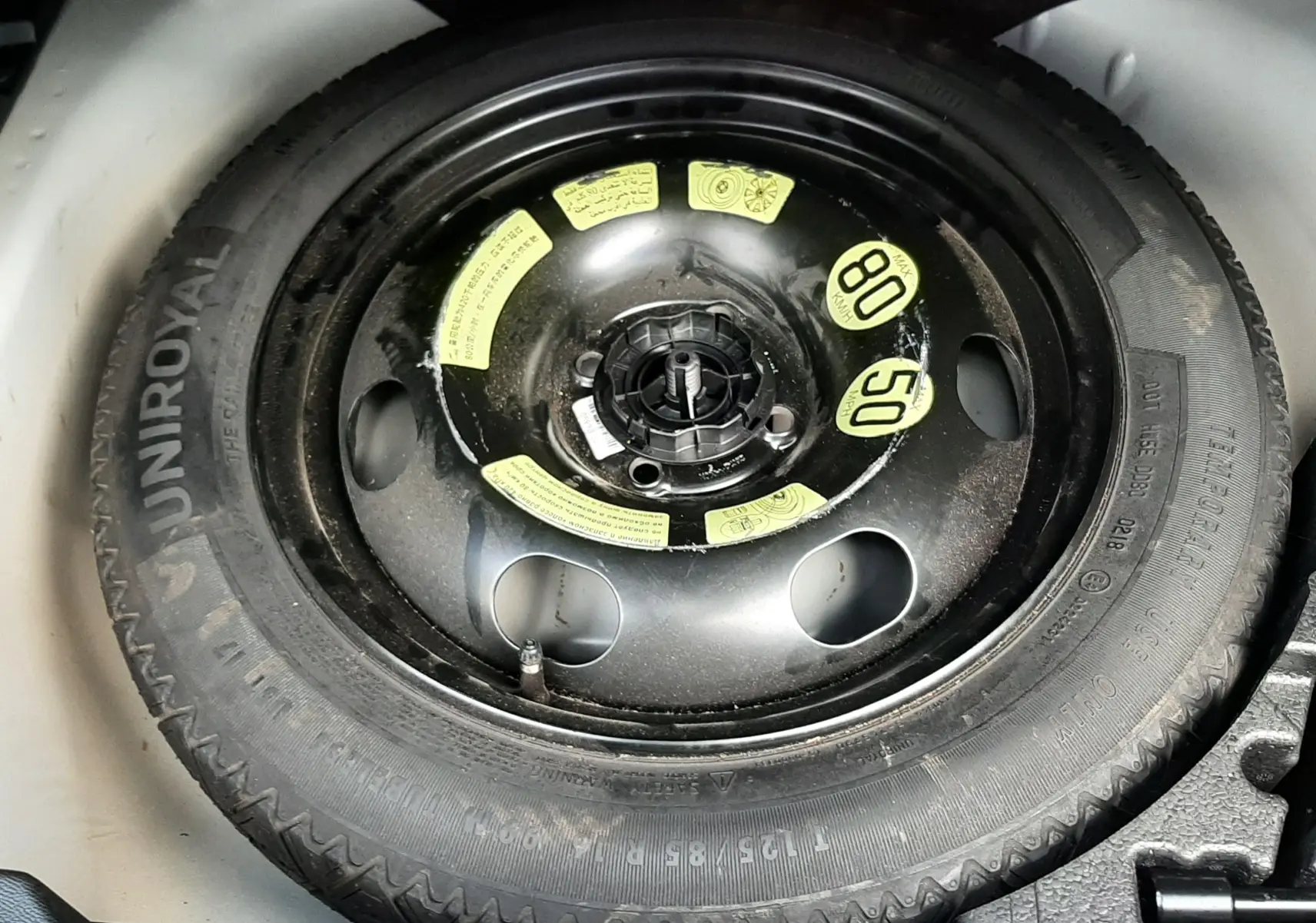 Roue de secours noire avec marquages jaunes dans le coffre d'un Peugeot 2008 blanc de 2021.