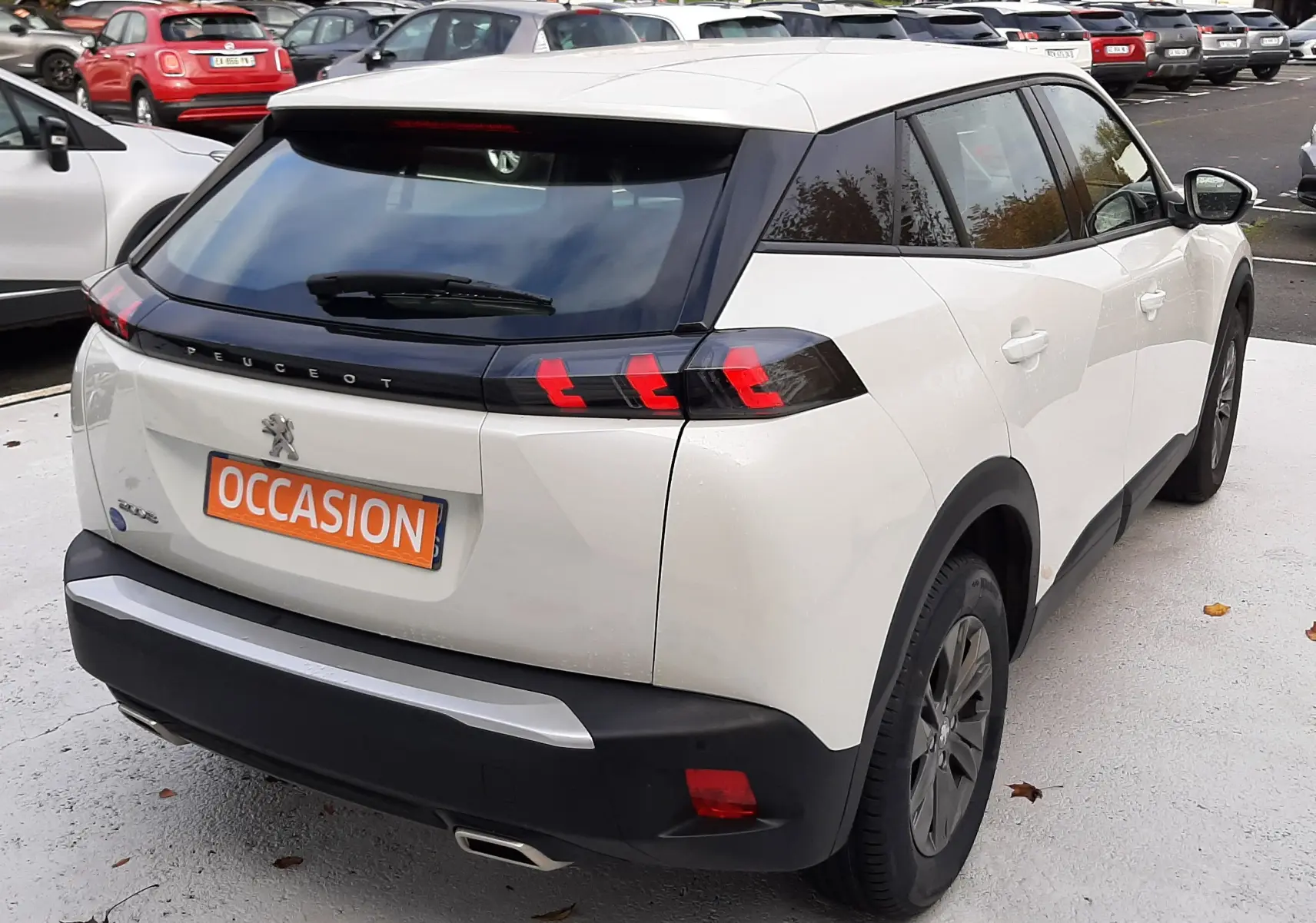 Vue 3/4 arrière droite d'un Peugeot 2008 blanc avec feux arrière LED et plaque "OCCASION" sur parking.