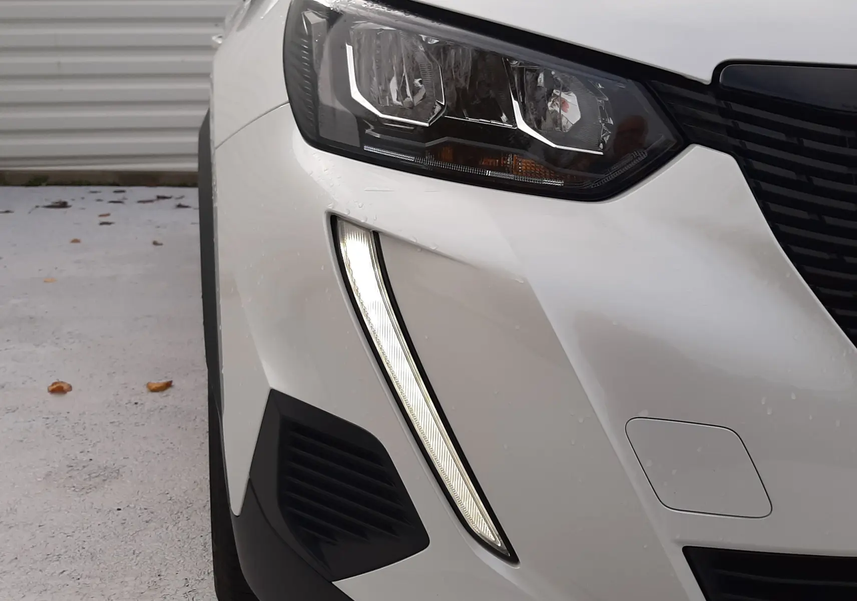 Gros plan sur l'avant droit blanc du Peugeot 2008 avec ses phares LED et la signature lumineuse verticale distinctive.