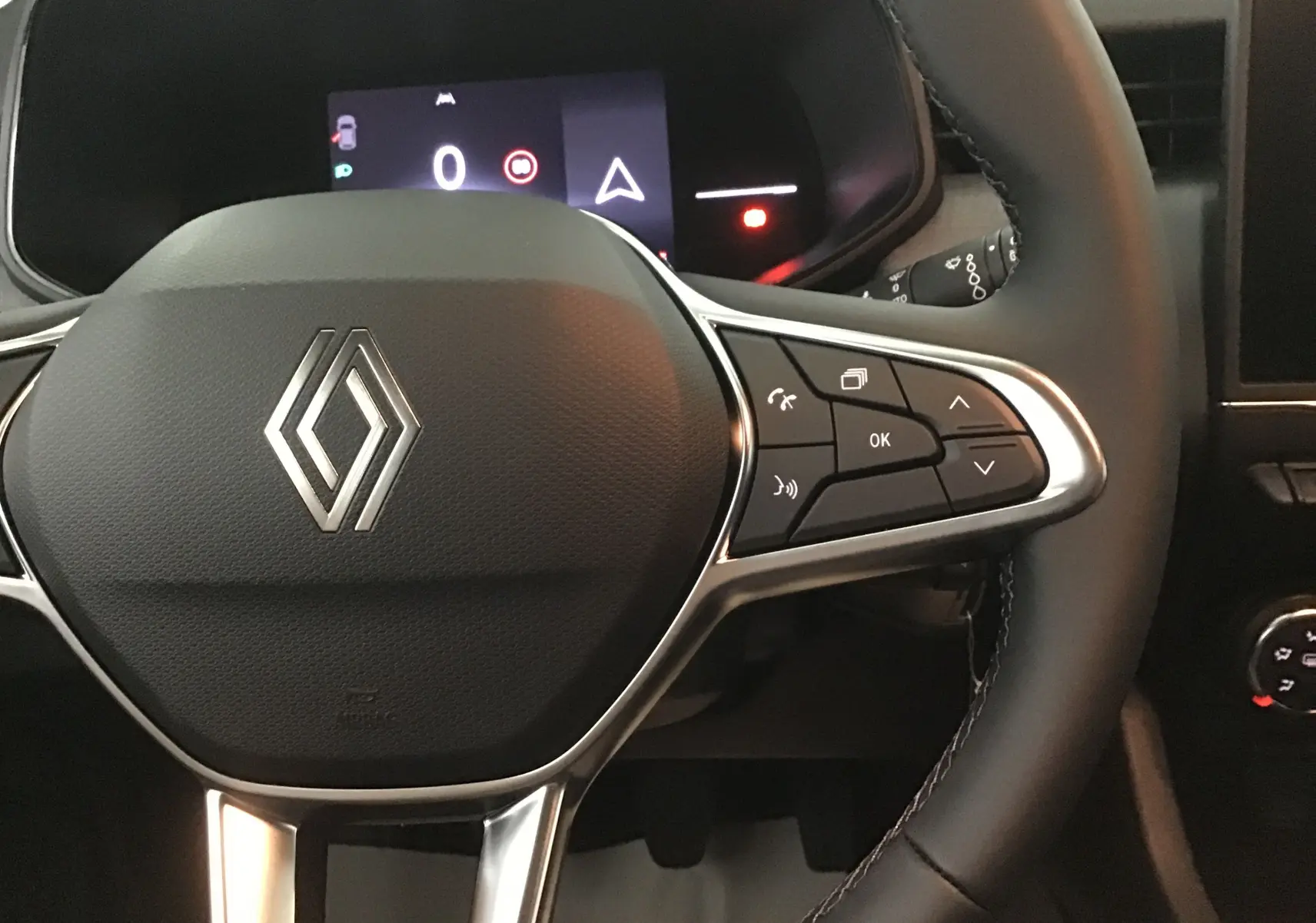 Vue rapprochée du volant de la Renault Clio V 2025 avec commandes intégrées et tableau de bord numérique allumé.