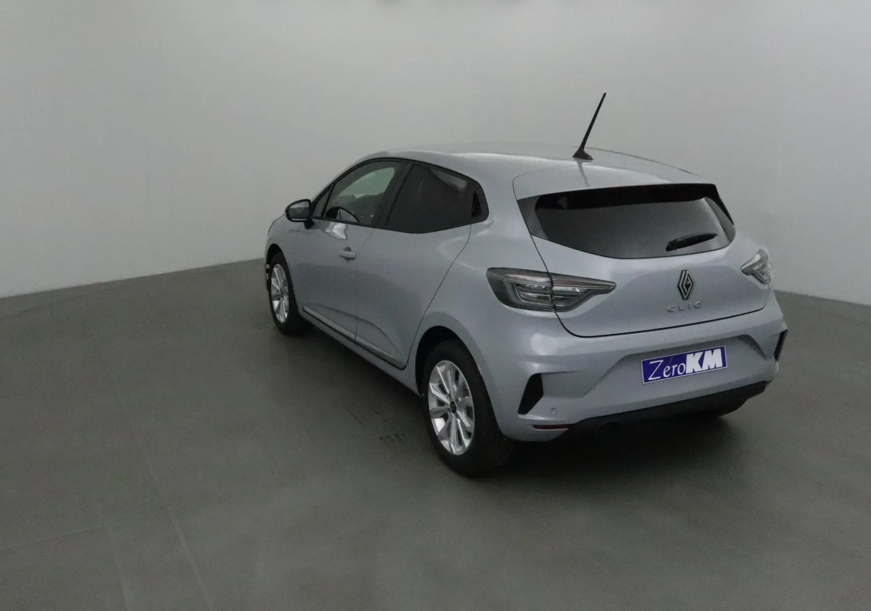 Vue 3/4 arrière gauche d'une Renault Clio V gris Rafale avec vitres teintées et protections latérales chromées.