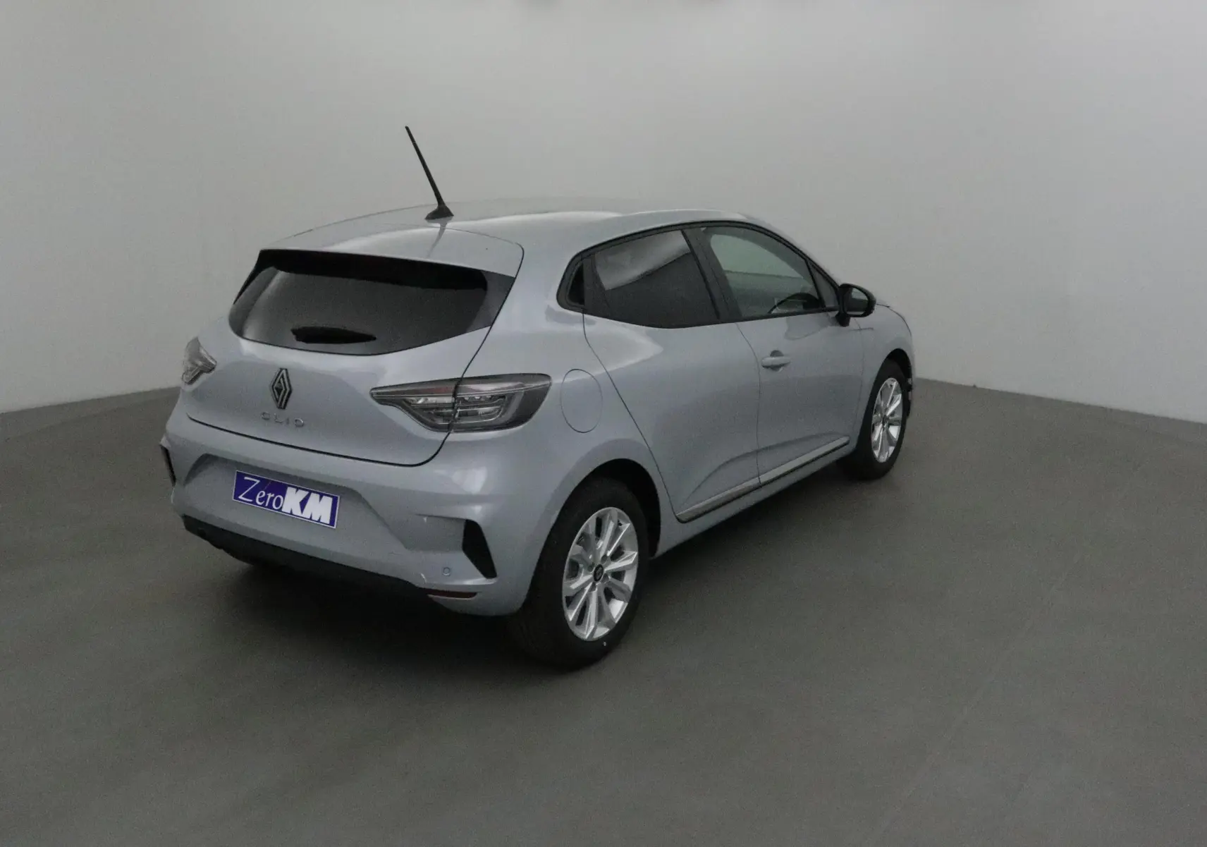 Renault Clio V gris Rafale vue 3/4 arrière droit, avec vitres teintées et protections latérales chromées visibles.