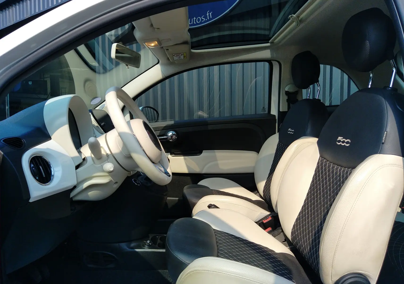 Intérieur de la Fiat 500 blanc, vue côté conducteur montrant les sièges cuir bicolores et le tableau de bord clair.