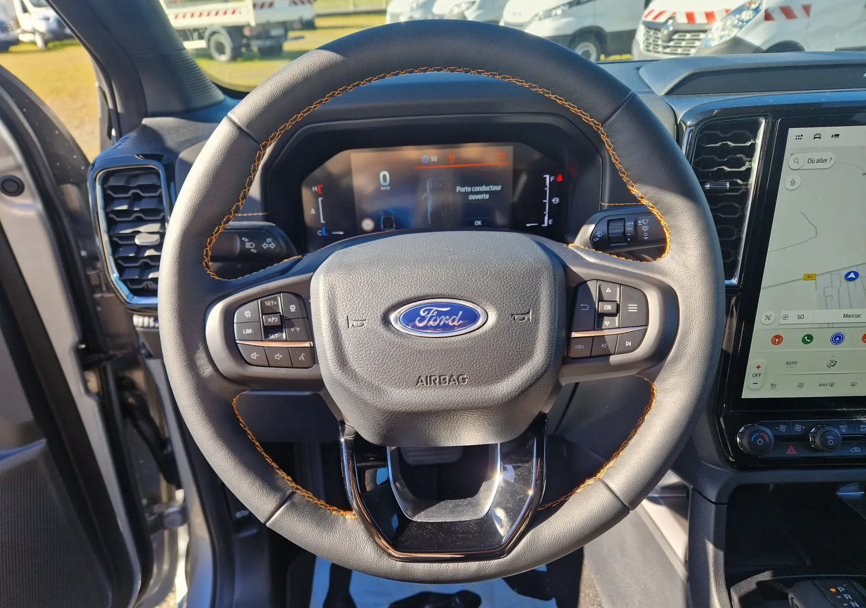 Vue rapprochée du volant en cuir noir avec surpiqûres orange du Ford Ranger Super Cabine gris Iconic, tableau de bord et écran tactile visibles.
