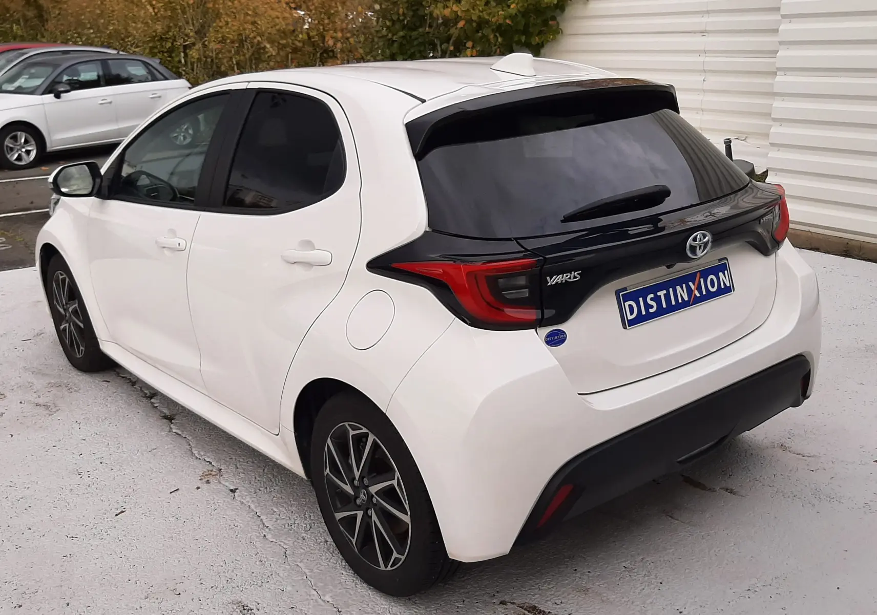 Vue 3/4 arrière droite d'une Toyota Yaris blanche 2023 avec toit et hayon noirs, jantes alliage bi-ton et vitres teintées.
