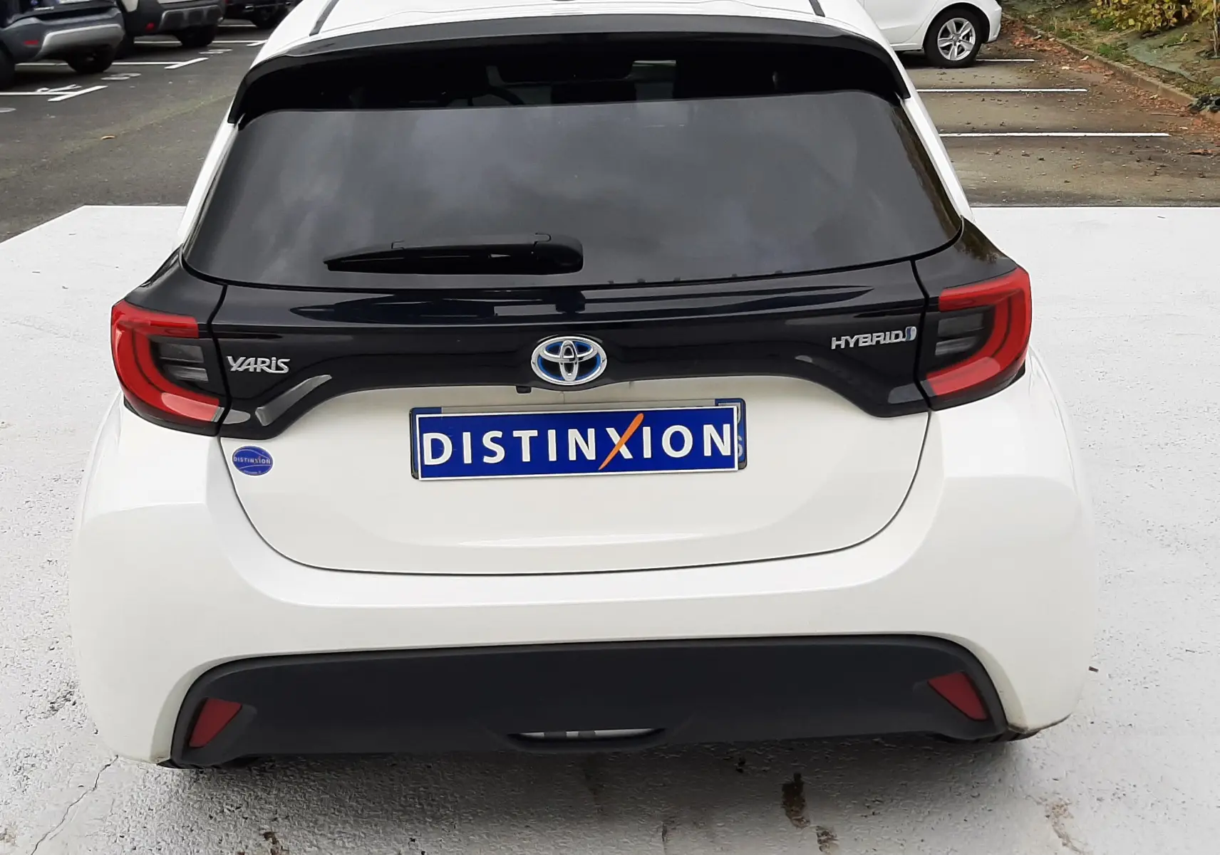 Vue arrière d'une Toyota Yaris blanche hybride 2023 avec toit noir et feux arrière rouges distinctifs.