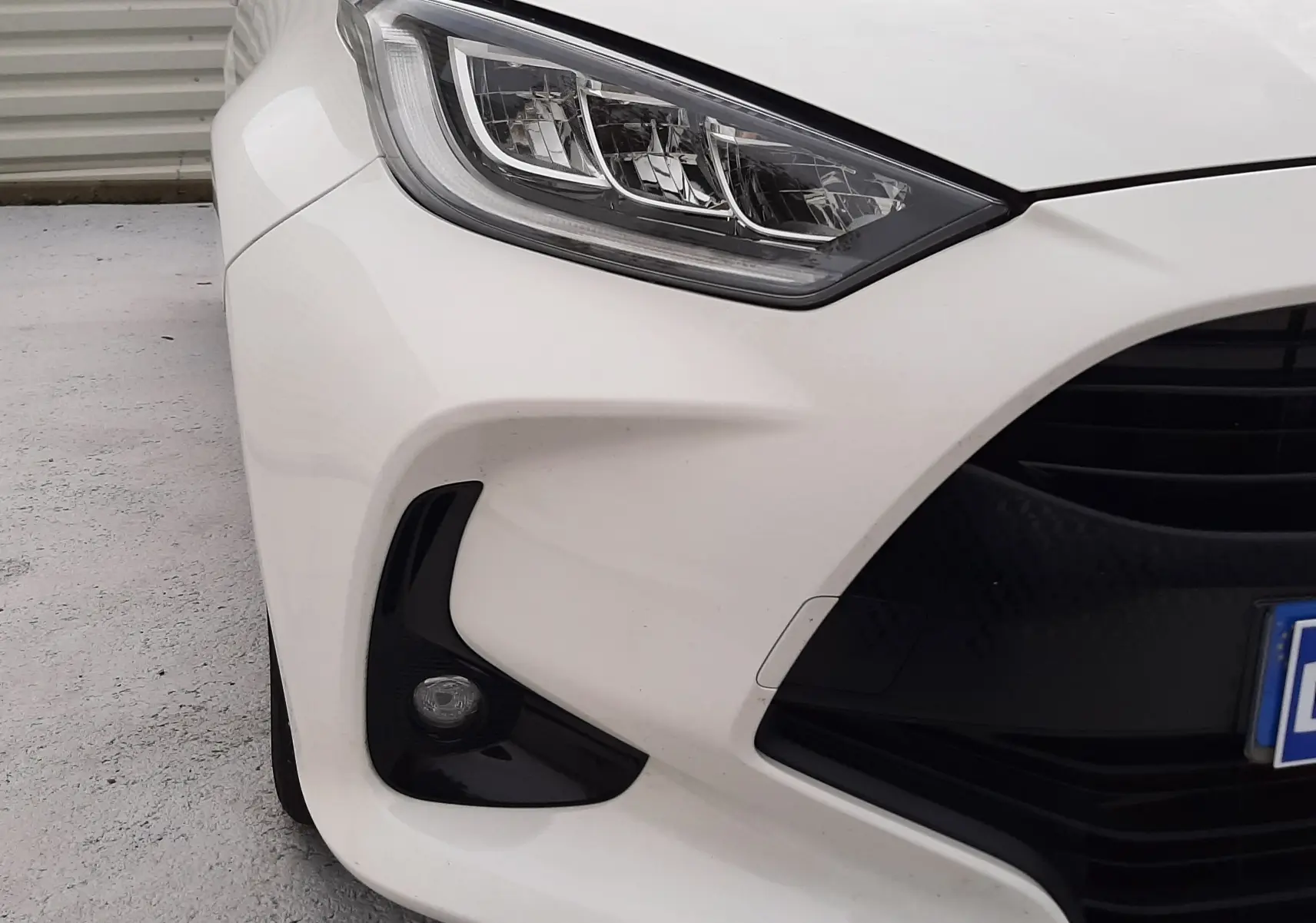 Gros plan sur l'avant droit blanc de la Toyota Yaris 2023, mettant en valeur le phare LED et le feu antibrouillard noir.