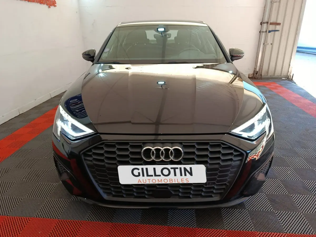 Vue frontale d'une Audi A3 noire 2022 avec calandre hexagonale et phares LED allumés en intérieur showroom.