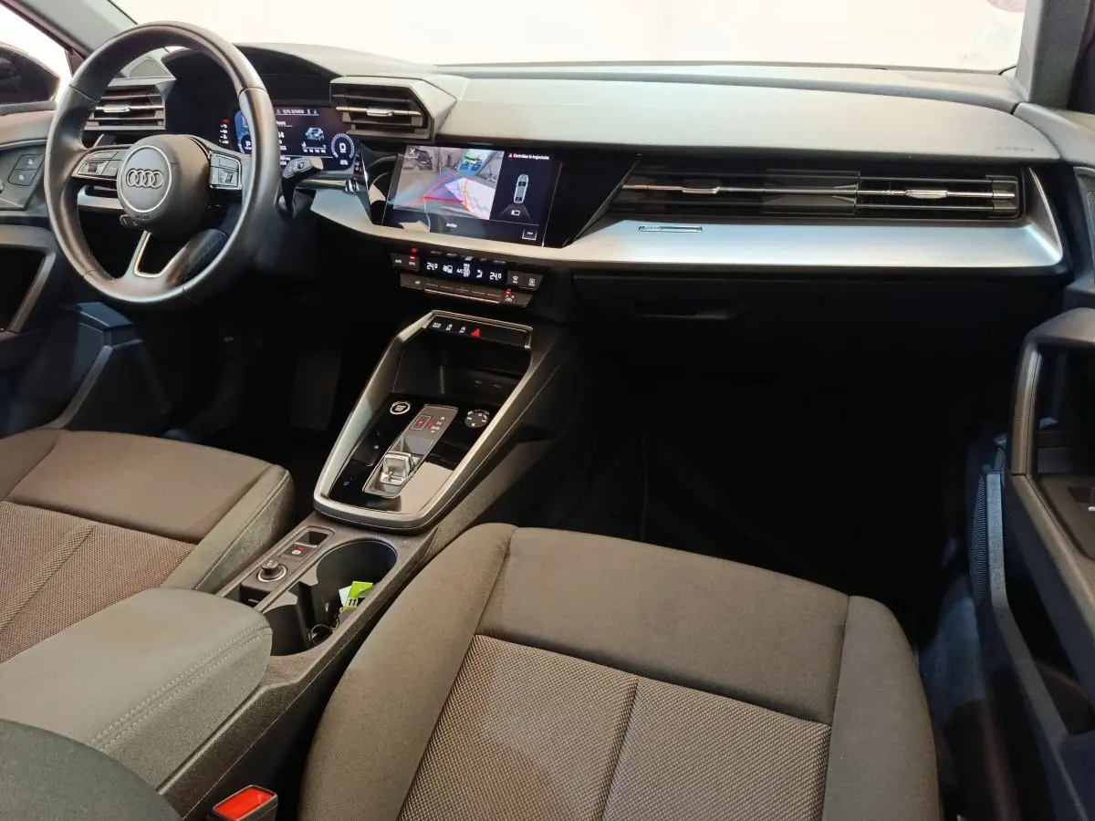 Intérieur de l'Audi A3 2022 noir, vue côté passager avant, tableau de bord moderne avec écran tactile et volant cuir.