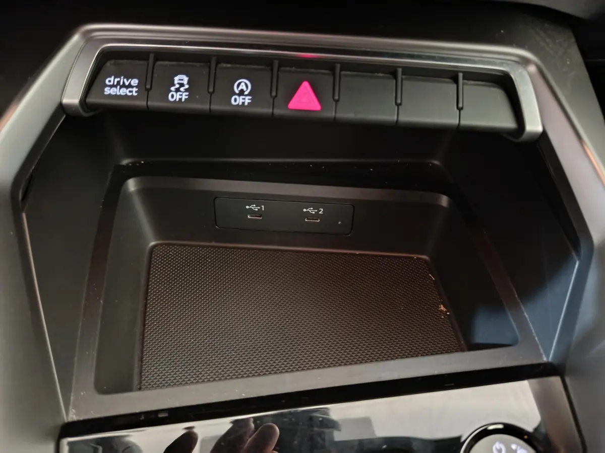 Vue rapprochée de la console centrale noire de l'Audi A3 30 TFSI MHEV avec ports USB et boutons de contrôle éclairés.