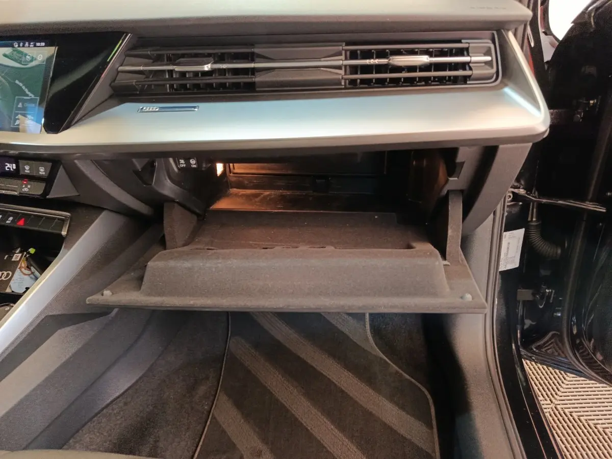 Vue intérieure côté passager de l'Audi A3 30 TFSI MHEV noire, boîte à gants ouverte et tableau de bord moderne.