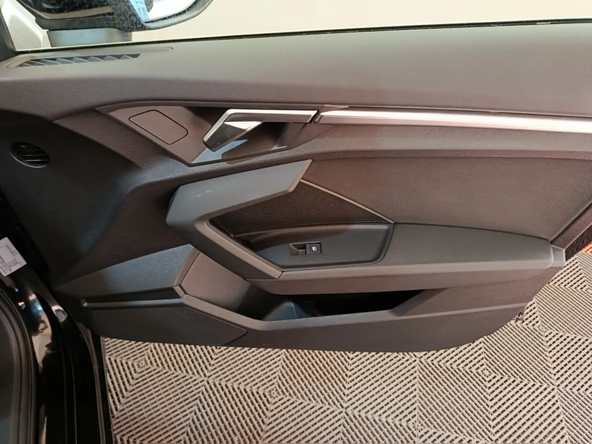 Vue rapprochée de la porte côté gauche noire de l'Audi A3 30 TFSI MHEV avec poignée argentée et commande de fenêtre.