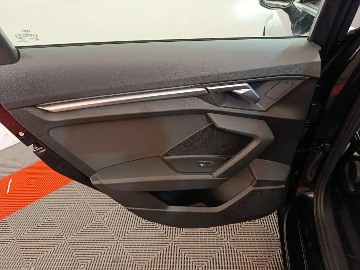 Porte intérieure côté gauche noire de l'Audi A3 30 TFSI MHEV Business Line 2022 avec poignée argentée et commande de vitre.