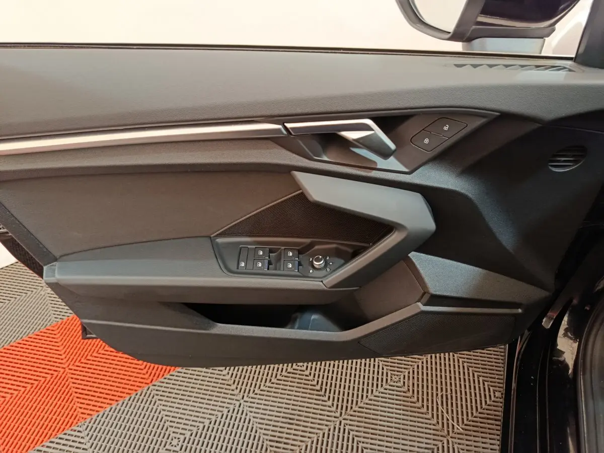 Vue rapprochée de la porte côté gauche noire de l'Audi A3 30 TFSI MHEV avec commandes de vitres et serrure intégrées.