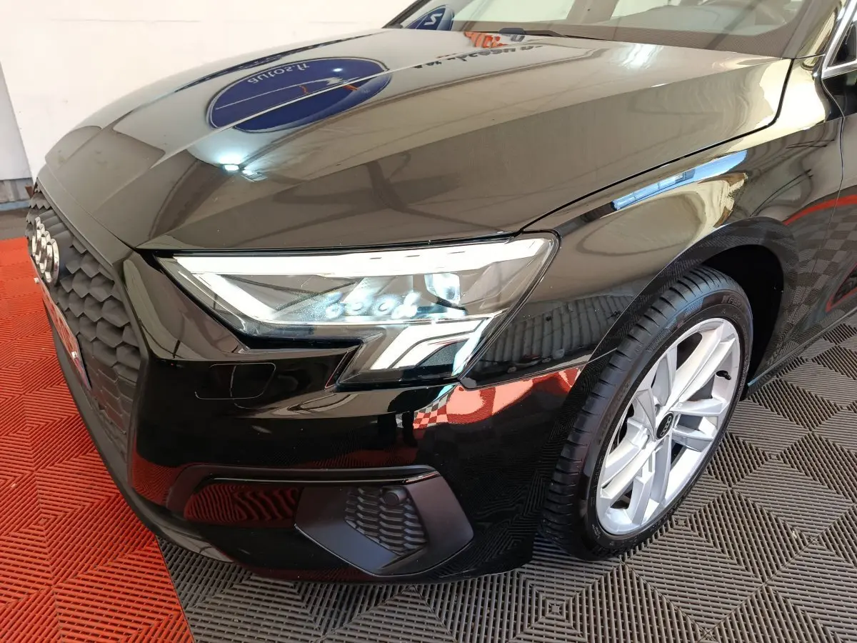 Vue 3/4 avant droit d'une Audi A3 noire 2022 mettant en valeur ses phares LED et sa calandre hexagonale distinctive.