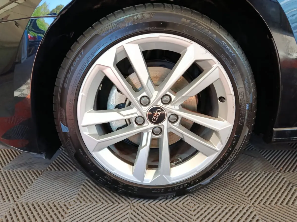 Gros plan sur la roue avant droite d'une Audi A3 noire, mettant en valeur la jante en alliage argentée à 5 doubles branches.