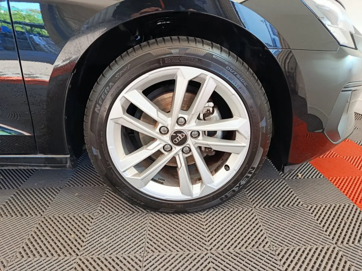 Gros plan sur la roue avant gauche d'une Audi A3 noire, mettant en valeur la jante alu à 5 doubles branches.