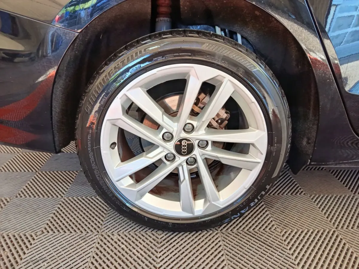 Gros plan sur la roue avant droite d'une Audi A3 noire, mettant en valeur la jante alliage argentée et le pneu Bridgestone.