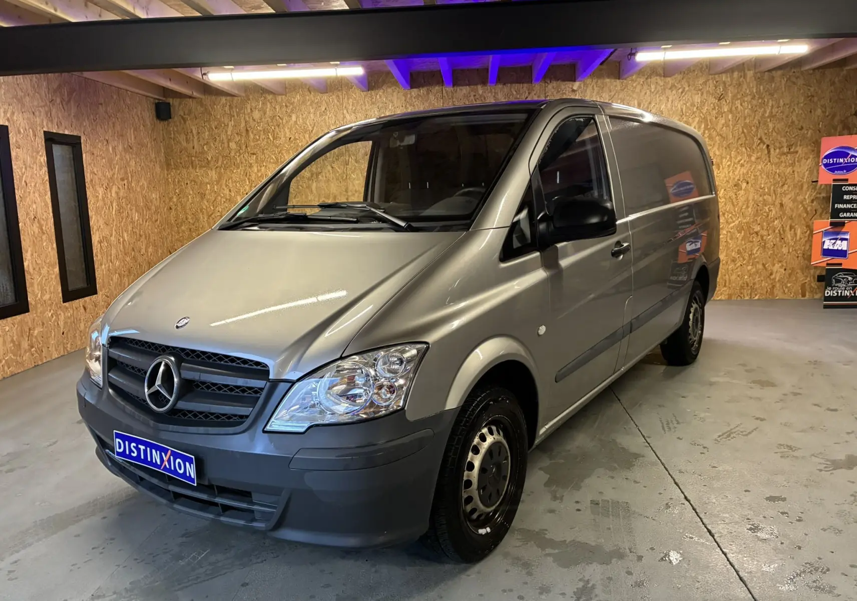 Fourgon Mercedes Vito gris en 3/4 avant droit dans un garage avec éclairage intérieur et plaques Distinxion.