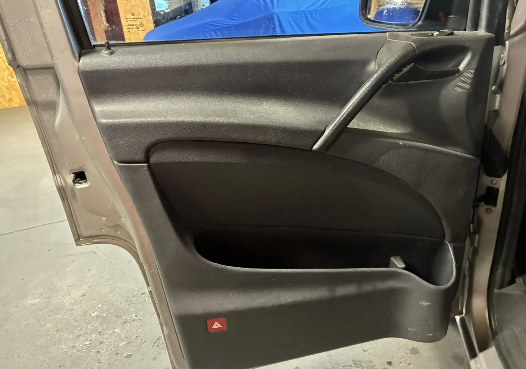 Vue intérieure de la porte avant gauche gris foncé du Mercedes Vito 2.8 113 CDI Fourgon Long, avec rangement et bouton de warning rouge.