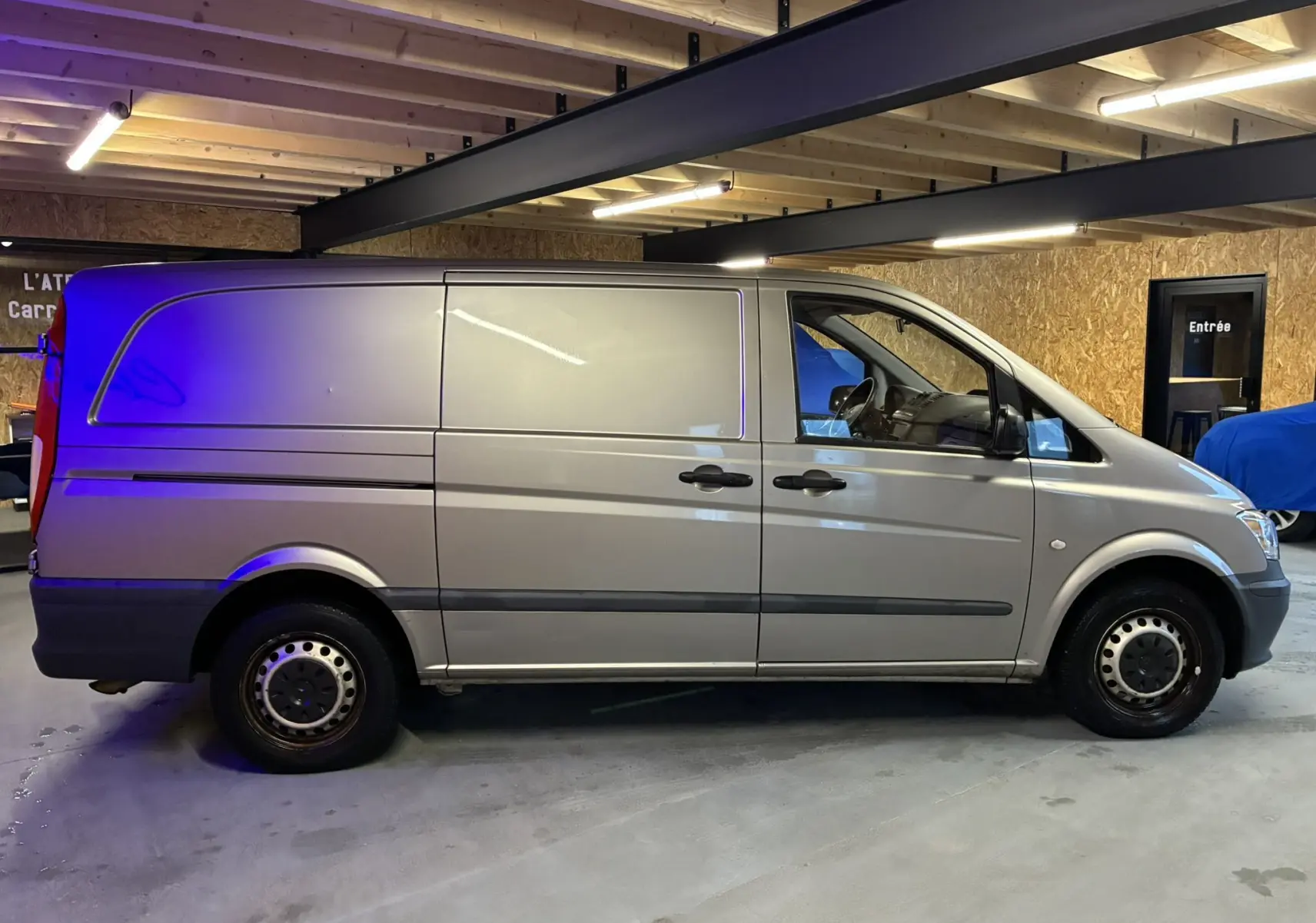 Vue de profil côté gauche d’un Mercedes Vito gris 2.8 113 CDI fourgon long, stationné en intérieur sous plafond en bois.