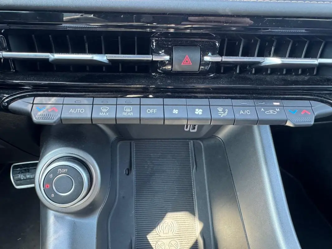 Vue rapprochée de la console centrale de l'Alfa Romeo Tonale 2025, avec commandes climatisation et molette de sélection de mode de conduite.