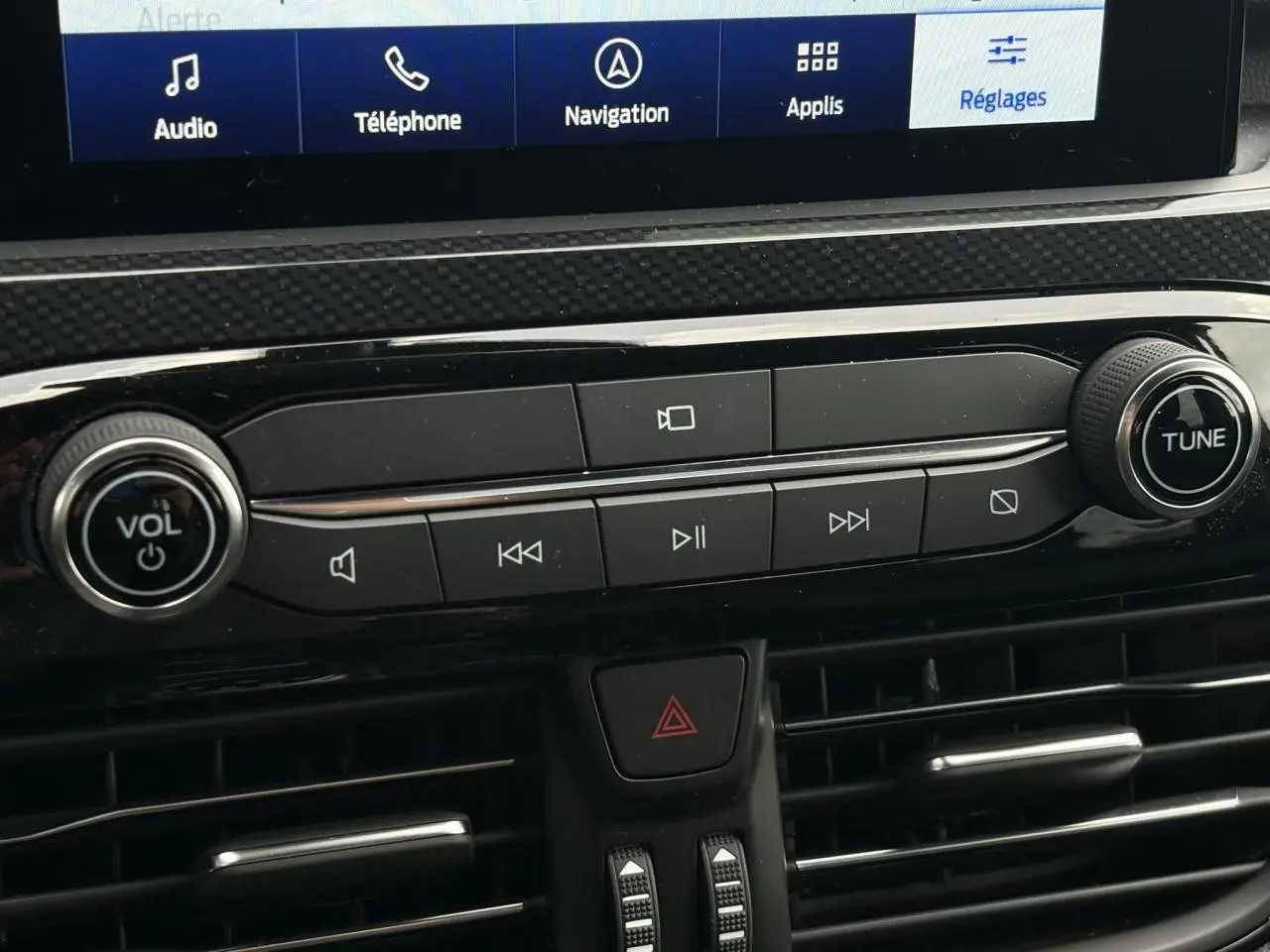 Gros plan sur la console centrale du Ford Kuga bleu azur 2023, avec commandes audio et écran tactile visible.