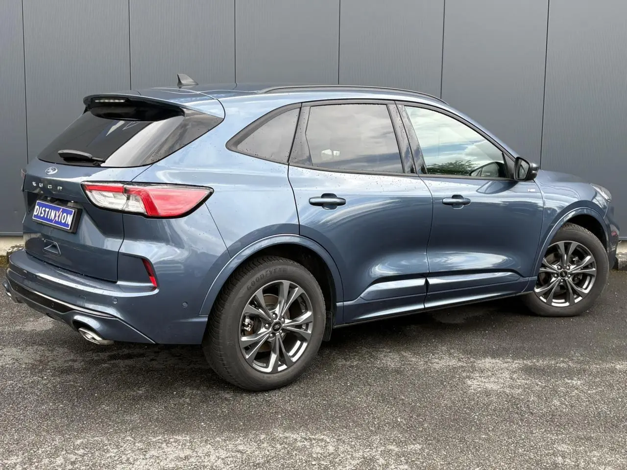 Vue 3/4 arrière droite d’un Ford Kuga 2023 bleu azur avec jantes alliage 18 pouces et double sortie d’échappement.