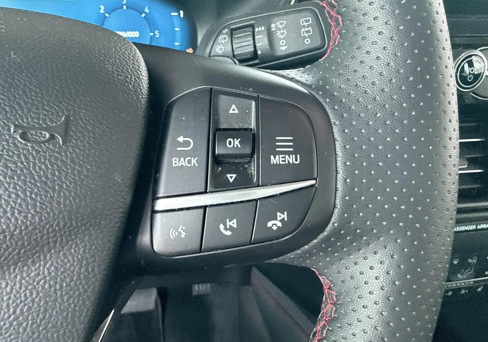 Gros plan sur le volant perforé noir avec surpiqûres rouges du Ford Kuga 2023, boutons de commande multifonctions visibles.