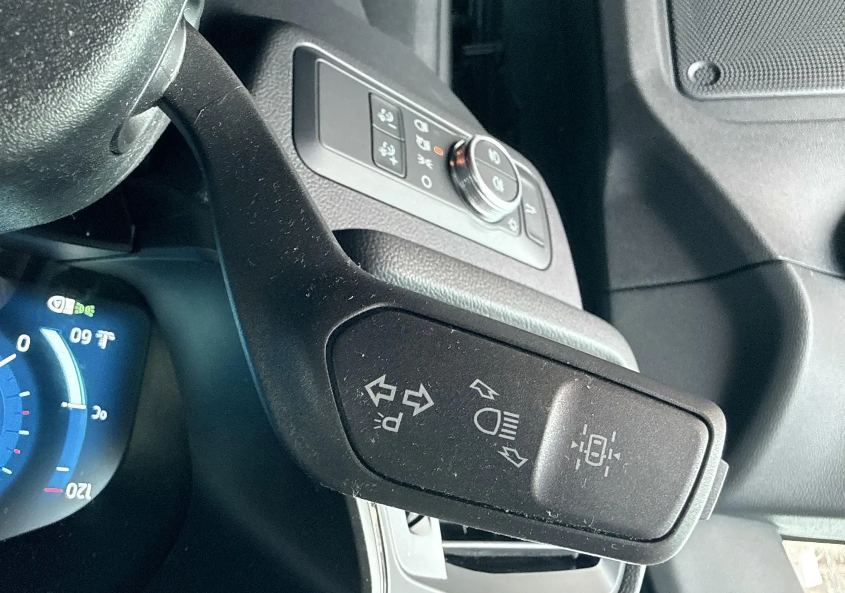 Gros plan sur la manette de clignotants noire à gauche du volant dans l'habitacle du Ford Kuga bleu azur 2023.