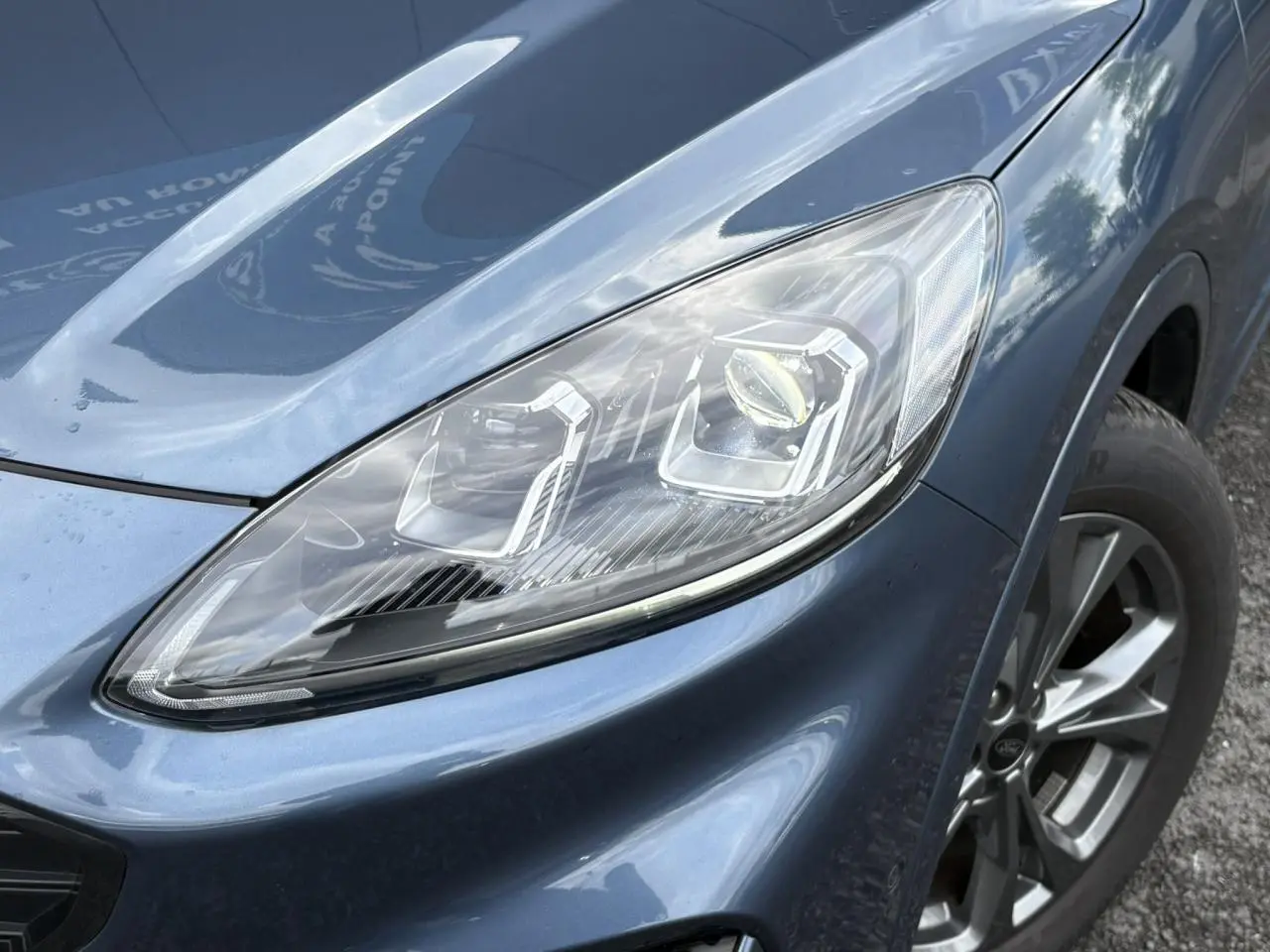 Gros plan sur le phare avant droit et la roue d’une Ford Kuga 2023 bleu azur finition ST-Line X.