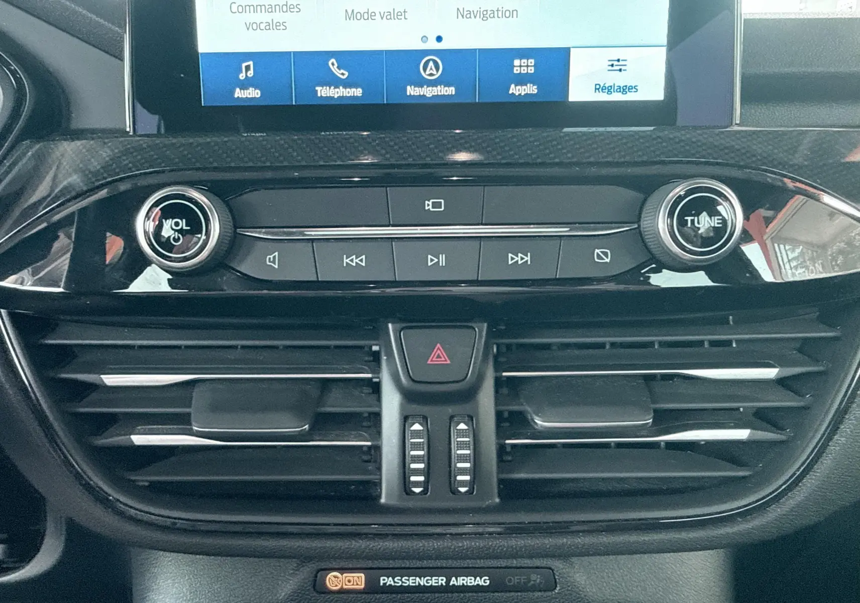 Détail de la console centrale noire du Ford Kuga 2023 avec commandes audio, écran tactile et aérateurs horizontaux.